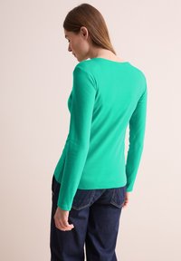 Dlouhá rukáv, fitted top v živé zelené barvě z bavlny, s kulatým výstřihem a hladkým povrchem, spárovaný s tmavě modrými džíny.