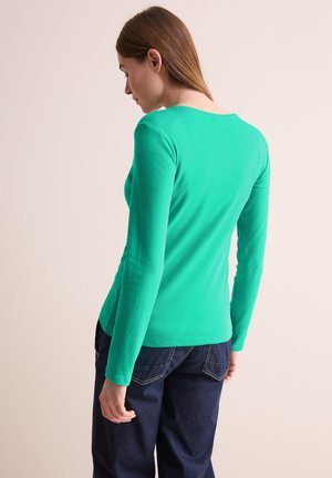 Dlouhá rukáv, fitted top v živé zelené barvě z bavlny, s kulatým výstřihem a hladkým povrchem, spárovaný s tmavě modrými džíny.