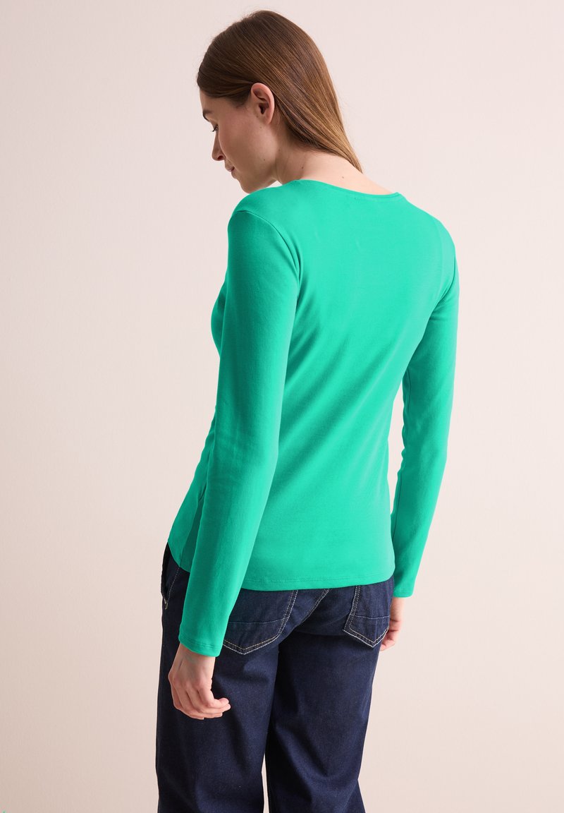 Dlouhá rukáv, fitted top v živé zelené barvě z bavlny, s kulatým výstřihem a hladkým povrchem, spárovaný s tmavě modrými džíny.