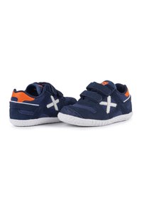 Sneaker in camoscio blu con accenti bianchi, doppie cinghie in Velcro, suola in gomma bianca texturizzata e dettaglio arancione sul tallone.