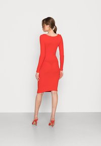 Vestido justo de manga longa vermelho feito de um tecido elástico, com costas em decote redondo, comprimento até ao joelho e uma silhueta elegante.