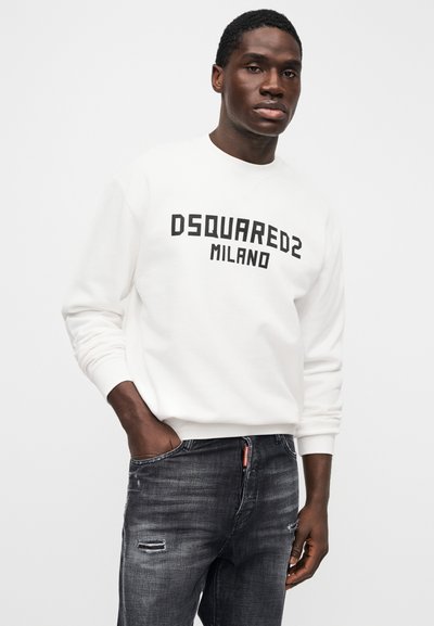 White sweatshirt with "DSQUARED2 MILANO" in bold black letters, worn with distressed dark jeans. Simple design, crew neckline, and long sleeves.