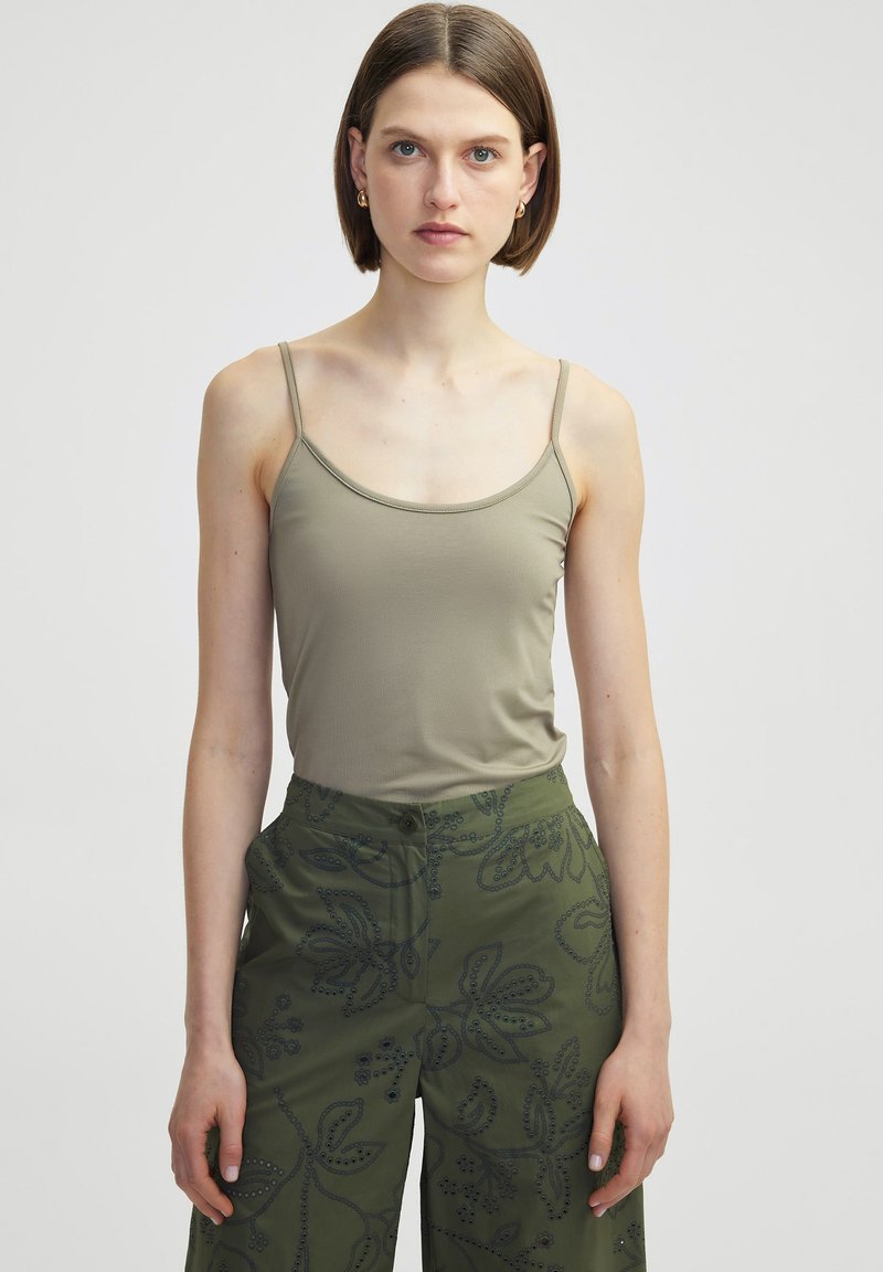 Olivgrünes, figurbetontes Tanktop mit dünnen Trägern, aus glattem Stoff gefertigt; kombiniert mit lockeren grünen Hosen mit floralen Stickereien und Nahtdetails.
