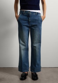 Jeans de tiro alto y pierna ancha en azul claro, con puños enrollados. Fabricados en denim, cuentan con bolsillos laterales y una etiqueta de marca en la cinturilla.
