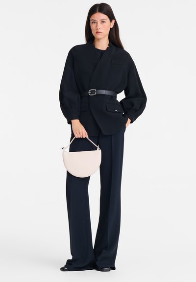 Schwarze übergroße Bluse mit V-Ausschnitt und aufgepufften Ärmeln, tailliert mit einem schwarzen Gürtel. Kombiniert mit marineblauen, weit geschnittenen Hosen und einer hellbeigen Handtasche.