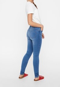 Blaue Skinny-Jeans mit hoher Taille, Seitentaschen und leichten Verwaschungen. Getragen mit einem weißen T-Shirt und roten flachen Sandalen.