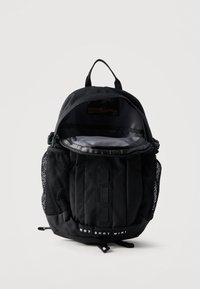 Μαύρο συμπαγές σακίδιο πλάτης με πλαϊνές θήκες από δίχτυ, ανοιχτό κύριο φερμουάρ και το κείμενο «Hot Shot Mini» στο κάτω μέρος μπροστά.