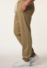 Beige Jogginghosen aus weichem Stoff, mit Seitentaschen, elastischem Bund mit Kordelzug und schmal zulaufenden Beinen, kombiniert mit weißen Turnschuhen.