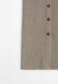 Gros plan sur un tissu tricoté côtelé beige avec trois boutons marron marbrés alignés verticalement.