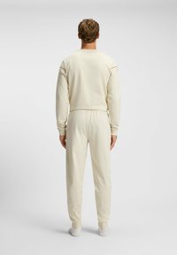 Crème-kleurige loungewear set met een langemouwen top en taps toelopende broek, beide met een gladde textuur en een elastische tailleband.