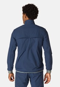Marineblaue Outdoor-Jacke mit hohem Kragen, dehnbarem Material, mit Reißverschluss versehenem Rückenbelüftungsbereich, elastischen Bündchen und reflektierenden Akzenten.