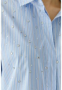 Light blue collared shirt with vertical white stripes, embellished with clear rhinestones across the fabric, offering a textured appearance.