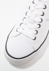 Weißer Leinencanvas-Sneaker mit rundem Zehenbereich, schwarzer Gummisohle und Metallösen. Verfügt über ein strukturiertes Obermaterial und flache Schnürsenkel für sicheren Halt.