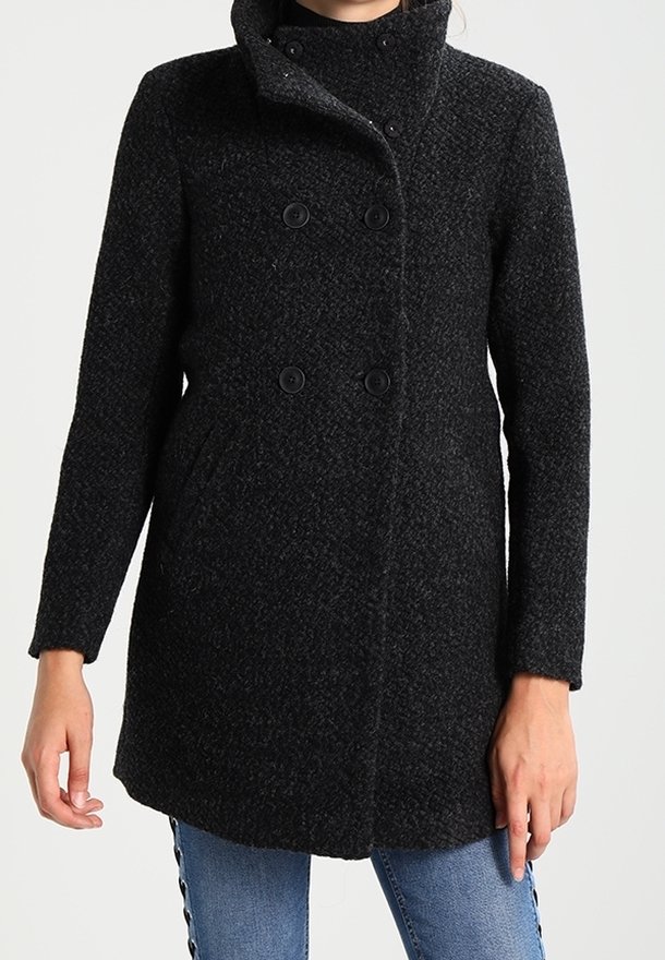 Femme portant un manteau texturé sombre à double boutonnage avec un col montant et des poches latérales, associé à un jean bleu.