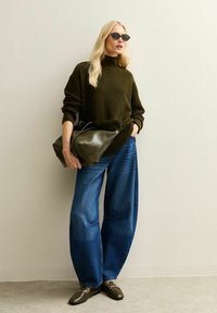 Übergroßer dunkelgrüner Pullover, weit geschnittene blaue Jeans, schwarze Sonnenbrille und eine große olivgrüne Handtasche. Glatte Textur und lässige Passform.