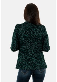 Blazer noir avec motif texturé bleu sarcelle, fermeture à un bouton, coupe ajustée et revers crantés, associé à un jean foncé.