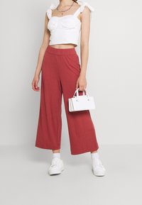 Femme portant un haut court blanc et un pantalon large rouge, tenant un sac à main blanc, avec des baskets et des chaussettes blanches.