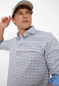 Hemd mit einem hellblauen Hintergrund und einem gepunkteten Muster in Blau und Creme, mit Knopfverschluss und kontrastierenden hellblauen Ärmeln.