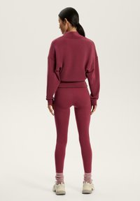 Set sportiv cărămiziu format dintr-un hanorac scurt, cu croială lejeră, și leggins mulați. Material moale cu manșete cu dungi și șosete contrastante.