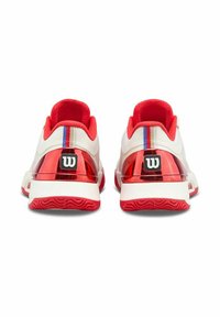 Zapatillas deportivas blancas y rojas con un talón rojo reflectante, parte superior de tela texturizada y una franja de acento azul. Presenta un logo negro en la parte trasera.