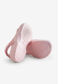 Roze rubberen slippers met een structuur op de zool en een cirkelvormig embleem op de band. De zolen zijn glad met een patroon voor grip.
