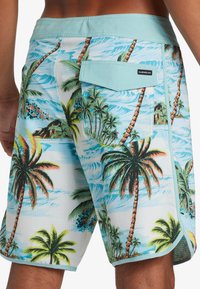 Colorful board shorts featuring a palm tree and ocean wave pattern, made of lightweight fabric with a mint green waistband and back pocket.