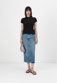 Zwarte poloshirt met gouden knopen, gecombineerd met een midi-lange blauwe denimrok. De outfit wordt aangevuld met bruine sandalen en een lichtpaarse tas.