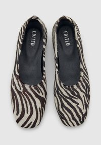 Een paar instappers met zwart-wit zebra print en zwarte binnenzolen met het label "EDITED," van bovenaf weergegeven op een witte achtergrond.