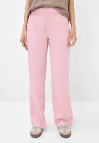 Lichtroze wijde broek met een elastische tailleband, gemaakt van een gladde stof. Gecombineerd met grijze en roze sneakers.