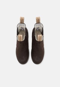 Botas de ante marrón sin cordones con suave forro blanco, paneles laterales elásticos y tiradores de cuero marrón con impresiones de logotipo en la parte trasera.