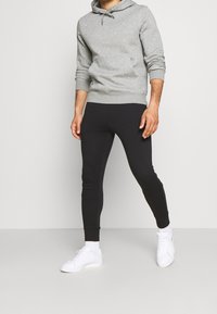Grå sweatshirt med huva och framficka, i kombination med svarta tajta joggingbyxor. Båda är gjorda av mjukt tyg och kompletteras av vita sneakers.