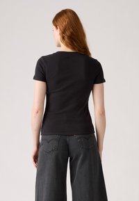 Maglietta nera a maniche corte con design aderente e scollatura rotonda, abbinata a jeans in denim grigio scuro a gamba larga con tasche posteriori.