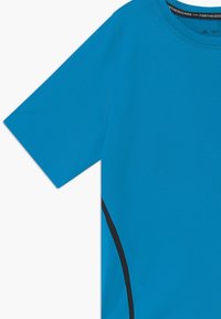 Camiseta deportiva azul de tejido texturizado, de mangas cortas, con cuello redondo y una franja lateral negra en contraste. Tejido suave.