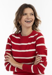 Maglione a righe rosse con spesse righe orizzontali bianche, design a girocollo e una texture morbida. Il modello posa con le braccia incrociate.