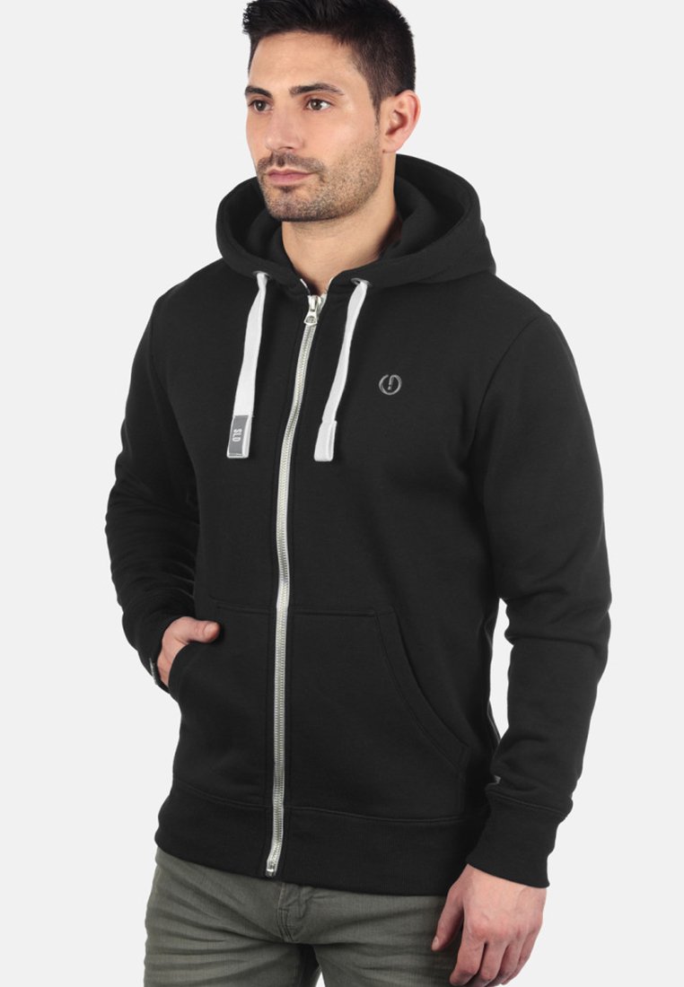 Zwarte ritshoodie met een voorzak, witte trekkoorden en een klein logo op de borst. Gemaakt van zachte, gewatteerde stof.