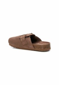 Zuecos de ante marrón, tipo slip-on, con una plantilla de corcho, presentando una correa asegurada por acentos metálicos redondos y una suela de goma texturizada.