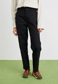 Pantalons noirs sur mesure avec une coupe droite, présentant une texture lisse et des passants de ceinture, associés à des chaussures de sport multicolores.