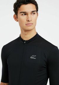 Maillot de cyclisme noir à manches courtes avec une fermeture éclair à l'avant, en tissu texturé, et un logo blanc sur la poitrine gauche. Coupe ajustée et design léger.