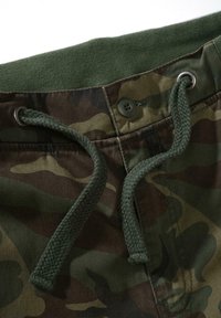 Kamufliažo šortai su žalia raišteliu ir liemene. Ypatybės: du metaliniai akių vožtuvai ir tekstūruotas audinys su žalia ir ruda raštų mišiniu.