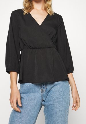 Blouse noire enroulée avec décolleté en V, taille froncée et manches 3/4, assortie à un jean taille haute bleu clair, en tissu lisse.
