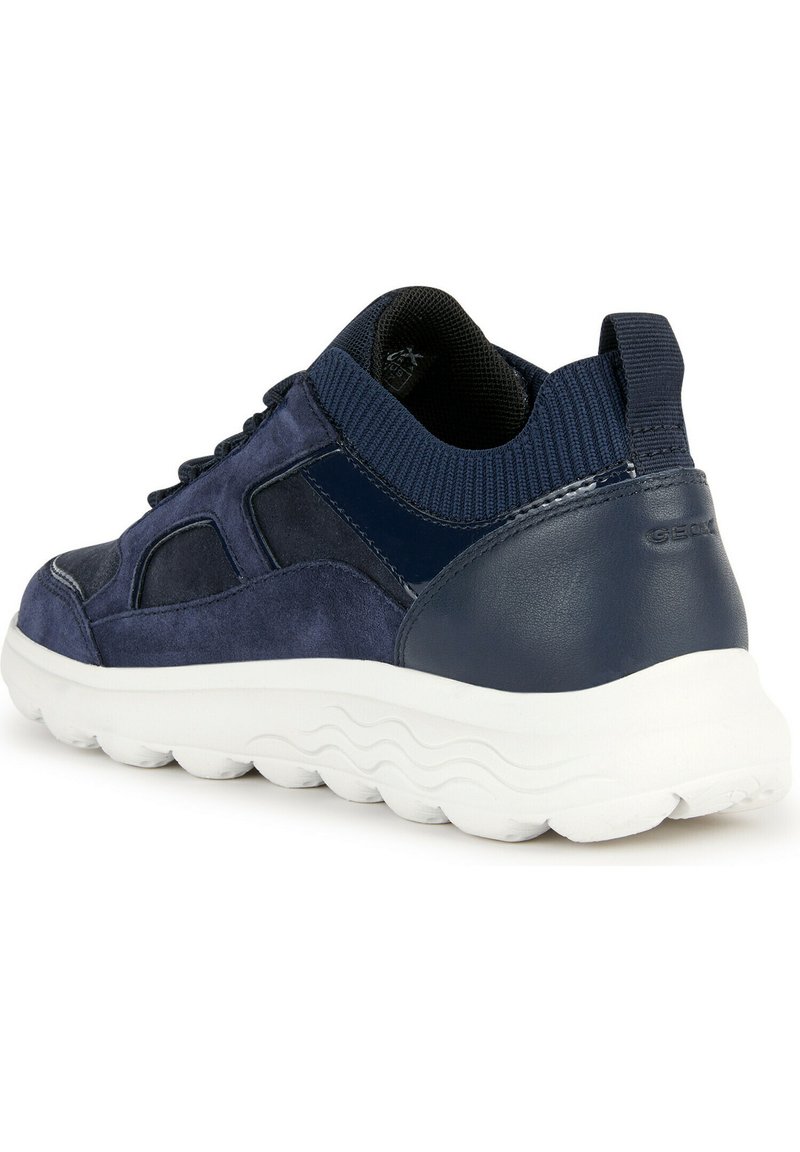 Zapatilla de ante y cuero azul con un cuello acolchado, superficie texturizada y una suela de goma blanca ondulada. Detalles reflectantes en el talón.