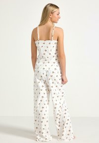 Biały komplet piżamowy składający się z topu na cienkich ramiączkach oraz luźnych spodni, oba zdobione zabawnym wzorem zwierząt. Miękka faktura tkaniny.