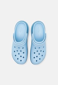 Lyseblå tresko laget av fleksibelt materiale, med dreneringshull og justerbar hælrem for sikker passform og ventilasjon.