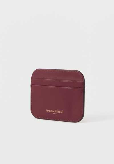 Κάρταholder από μπορντό δέρμα με τέσσερις θήκες, λεία υφή και χρυσό ανάγλυφο λογότυπο. Μινιμαλιστικός σχεδιασμός με στρογγυλεμένες γωνίες.