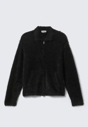 Veste zippée noire en tissu doux et moelleux. Comprend un col, une fermeture éclair et des poches latérales. Conçue avec une coupe courte.