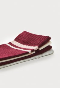 Drei Paar Socken im Pack: maroon mit pinken und weißen Streifen, einfarbig creme und hellgrau. Rippstruktur, weiches Strickmaterial.