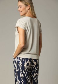 Haut gris clair à manches courtes en matière douce, associé à un pantalon marine à motifs avec des accents crème. Coupe décontractée, détails minimaux.