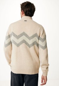 Beige gebreide trui met een hoge kraag, voorzien van een grijs-wit zigzagpatroon op de achterkant, ribbels aan de mouwen en onderkant.