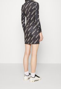 Robe noire à manches longues ornée de logos Adidas blancs et d'un tissu texturé. Associée à des baskets Adidas noires et blanches ainsi qu'à des chaussettes blanches.