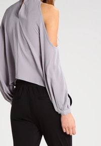 Haut court gris clair avec design à épaules dénudées, texture plissée et col montant, associé à un pantalon noir à taille élastique.